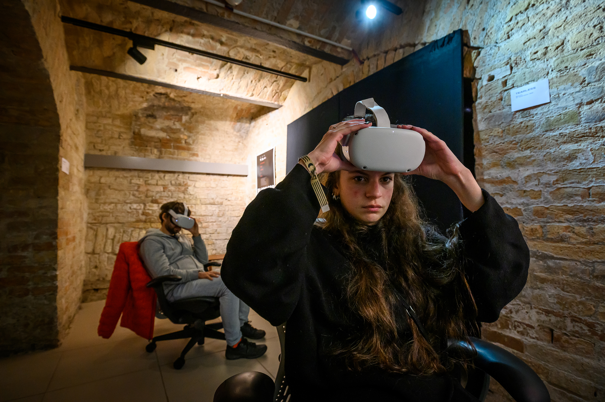 girl putting on a virtual reality headset and a man watching a VR film in the background
