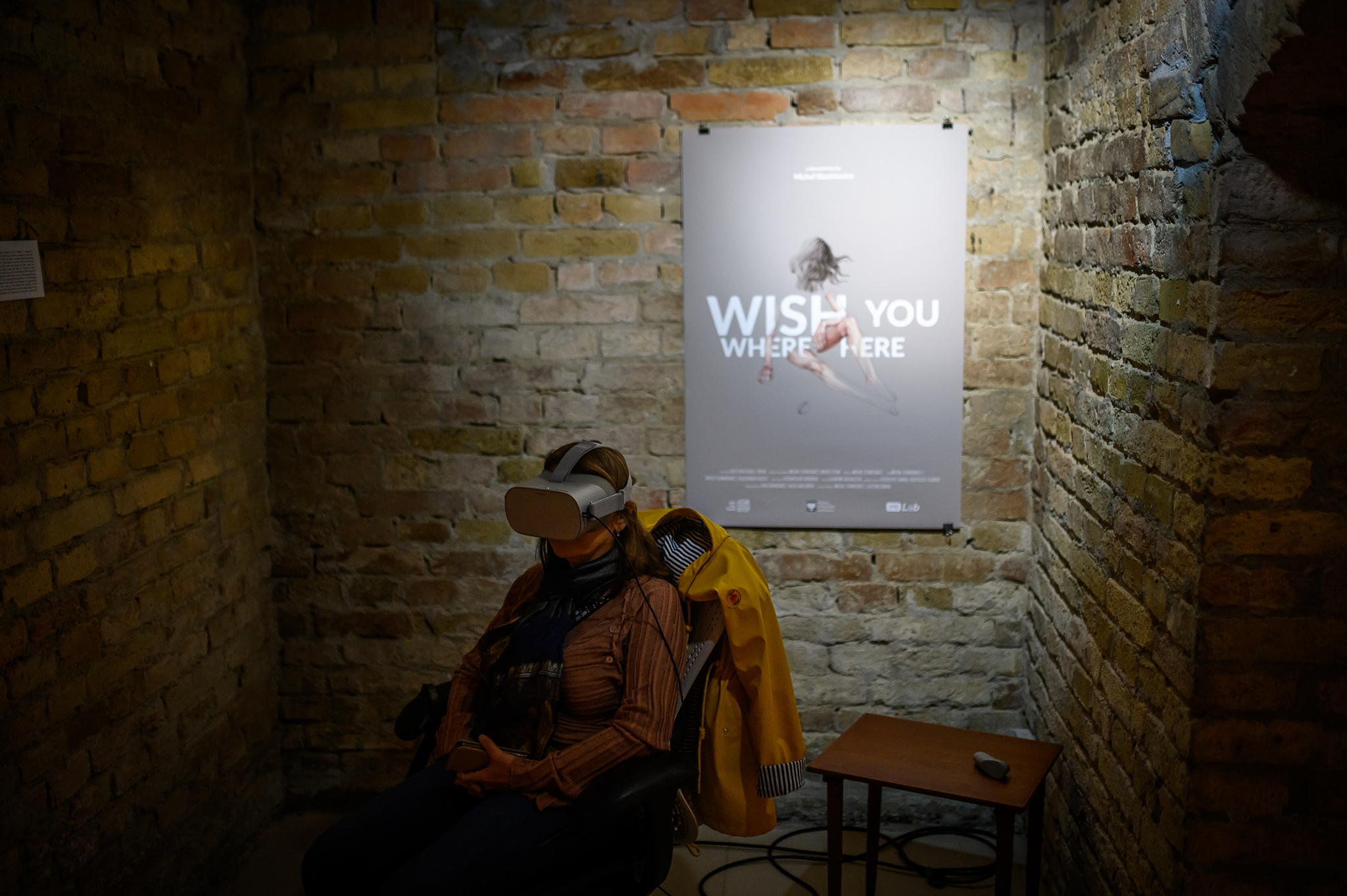 A poster of a virtual reality film Wish you were here and a woman sitting in front of it in a VR headset